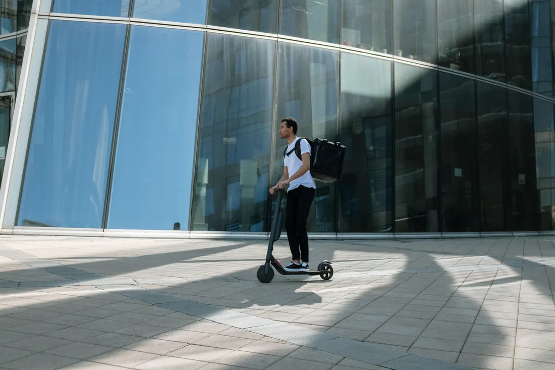 Trottinette électrique : quelle assurance pour rouler serein ? 1 Courtier Assurances et Financements Rennes Assurance trottinette électrique : utilisateur en trottinette électrique avec sac à dos devant un immeuble urbain, engagé sur la voie publique